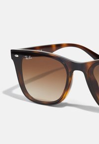 Ochelari de soare cu model țestoasă, cu lentile maro cu degradeu, formă rectangulară, accente negre și logo-ul Ray-Ban pe rama aproape de lentilă.
