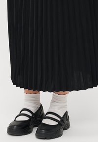 Svart plisserad kjol i kombination med svarta Mary Jane-skor med dubbla remmar. Vita ribbade strumpor med scalloped kanter syns.