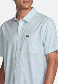 Short-sleeve button-up shirt in light blue with a floral pattern, featuring a chest pocket and a small RVCA logo on the left side.