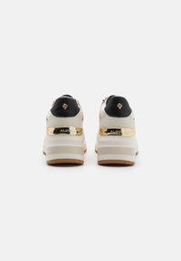 Weiße und schwarze Sneakers mit einer klobigen Plattform, goldenen Akzenten und einem strukturierten Rückenteil. Enthält ein Logo an der Ferse und glatte Materialien.