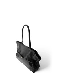 Sac cabas en cuir noir avec de longues anses, un détail de ceinture fine avec une petite boucle dorée à l'avant, et une forme souple légèrement affaissée.
