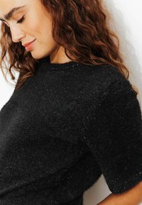 Pull noir à manches courtes en matière douce et texturée avec des paillettes discrètes. Il présente un col rond et une coupe décontractée.