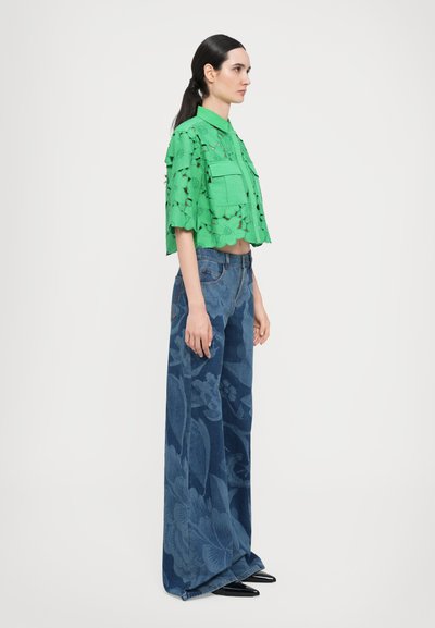 Green floral lace crop shirt with two front pockets, paired with high-waisted blue denim jeans featuring a dark floral pattern.
