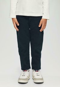 Dunkelgrüne Baumwollhosen mit Slim-Fit-Schnitt. Kombiniert mit weißen Sneakers mit grauen Akzenten und einer strukturierten Sohle.