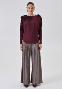 Maglione bordeaux con ruffles texture sulle spalle, abbinato a pantaloni a gamba larga a quadri in toni neutri. Tessuto morbido, vestibilità sartoriale.