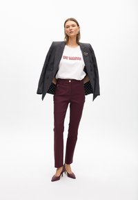Blazer de corte cruzado de rayas grises sobre camiseta blanca con texto rojo, combinado con pantalones slim-fit burdeos y tacones altos ciruela.