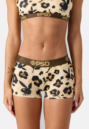 Kvinde iført beige og sorte undertøjsshorts med blomsterprint og matchende bh med brune PSD-brandede elastiske bånd.