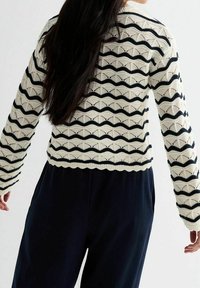 Maglione lavorato a maglia in crema con righe a zigzag nere, caratterizzato da un design cropped e maniche lunghe. Il motivo a traforato aggiunge texture.