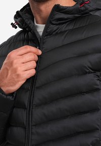Sort pufferjakke har et quiltet design, en lynlås lukning og en hætte med justerbare toggle-funktioner. Blød tekstur og strømlinet silhuet.