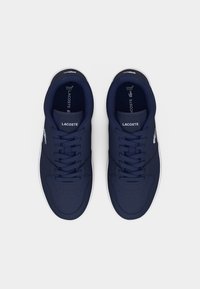 Paire de baskets Lacoste bleu marine avec logo et lacets blancs, vue de dessus sur un fond blanc uni.
