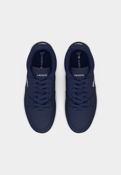 Двойка маратонки Lacoste в тъмносиньо с бяло лого и връзки, гледани отгоре на обикновен бял фон.