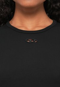 Fekete, testhez simuló felső kerek nyakkivágással, középen elhelyezett kivágásos részlettel és texturált logó díszítéssel.