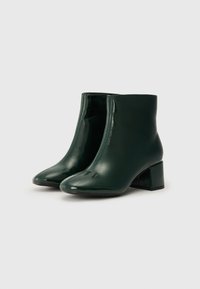 Bottines en cuir verni vert à talon bloc, avec un design épuré et une texture lisse et brillante. Aucune motif ou élément de quincaillerie visible.