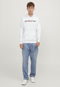 Hvit hettegenser med frontlomme, "JACK & JONES"-logo i svart. Kombinert med lyseblå baggy jeans og hvite joggesko.