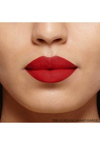 Application de rouge à lèvres rouge mat sur des lèvres pulpeuses, mettant en avant une texture lisse et une forme bien définie. Accompagné du nom du produit en dessous.