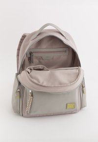 Hellgrauer Rucksack aus glattem Stoff, mit einem oberen Griff und mehreren Reißverschlussfächern, darunter eine Innentasche und ein gemusterter Reißverschlussanhänger.