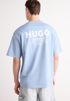 T-shirt azzurro chiaro a maniche corte con logo bianco "HUGO" e testo sul retro. Tessuto in cotone morbido con vestibilità comoda.