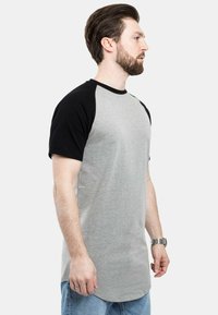 Harmaa ja musta raglan-paita, jossa on lyhyet hihat, pyöreä helma ja pehmeä puuvillasekoitemateriaali. Yksinkertainen muotoilu ilman kuvioita.