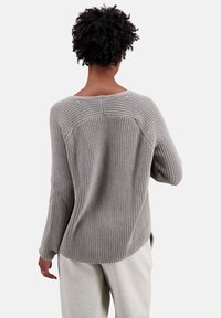 Pull en tricot gris clair avec une coupe décontractée, doté d'un col arrondi, d'une texture côtelée et de manches longues. Les fentes sur les côtés améliorent le confort.