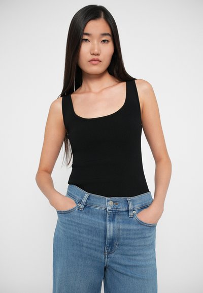 Sort ribbet bodystocking med brede stropper, parret med lyseblå højtaljede jeans med afslappet pasform og forlommer, glat tekstur.
