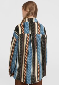 Multi-colored flannel shirt featuring herringbone patterns in blue, brown, and cream, with a relaxed fit and collar. Textured fabric.