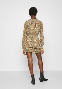 Mekko, jossa on leopardikuosiset pitkät hihat, korostettu vyötärö, kerroksellinen röyhelöhelma ja avoin selkäyksityiskohta. Yhdistetty mustiin nilkkasaappaisiin.