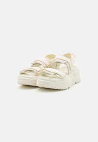 Sandalias deportivas blancas con correas transparentes, cierres ajustables de Velcro, suelas gruesas acolchadas y una banda de rodadura texturizada para mayor agarre.
