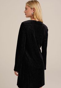 Black velvet dress with long sleeves, featuring a smooth texture and a straight cut. Back view showcases a simple, elegant silhouette.