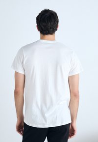 White cotton t-shirt with a rounded neckline and short sleeves, viewed from the back. Features a relaxed fit and smooth texture.