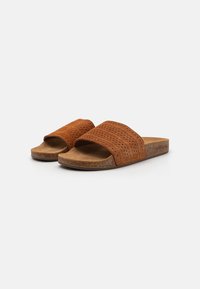 Sandali marroni slip-on con due cinghie testurizzate, una soletta in sughero e una suola piatta, progettati per il comfort e l'uso quotidiano.