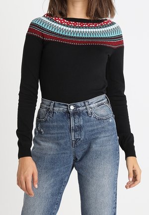 Schwarzes Langarmoberteil mit einem bunten, gemusterten Einsatz in Rot, Türkis und Schwarz, kombiniert mit hoch taillierten, leicht verwaschenen blauen Jeans.