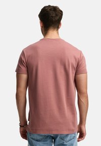 Camiseta de manga corta y cuello redondo en algodón color rosa polvo con una textura suave. Diseño minimalista, sin patrones ni logotipos visibles.