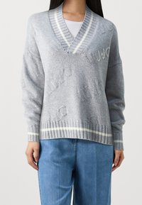 Grauer Strickpullover mit V-Ausschnitt, mit erhabenen Markenbuchstaben und weiß gestreiftem Rippstrick am Kragen und Saum. Locker geschnittenes Design.