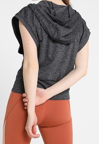 Grå ärmlös hoodie med texturerad yta, utrustad med huva och en avslappnad passform, kombinerad med rostfärgade leggings.