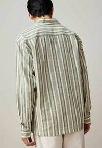 Gestreiftes Langarmhemd mit abwechselnd grünen und beigen Streifen. Hergestellt aus leichtem Stoff, mit lockerer Passform undKnopfmanschetten.