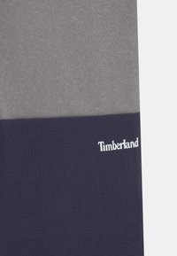 Szary i granatowy sweter colorblock, z miękką teksturą, prążkowaną dolną częścią oraz białym logo "Timberland".