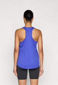 Μπλε αθλητικό τοπ με σχεδιασμό racerback, κατασκευασμένο από ελαφρύ ύφασμα, σε συνδυασμό με εφαρμοστά μαύρα σορτς, ομαλή υφή.