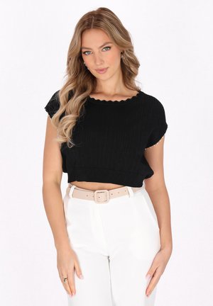 Schwarzes geripptes Cropped Top mit gewelltem Ausschnitt, kombiniert mit weißen hochgeschnittenen Hosen und einem hellbeigen Gürtel. Glatte Stofftextur.