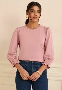Rosa Bluse mit rundem Ausschnitt und Rüschensaum, ausgestattet mit Puffärmeln und elastischen Bündchen sowie dekorativen Stickdetails.
