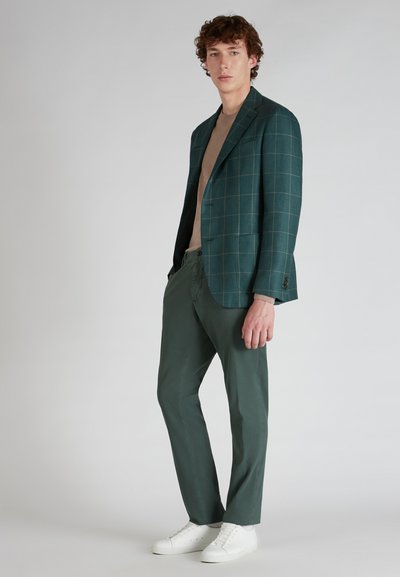 Blazer a quadri verde scuro con vestibilità sartoriale, abbinato a pantaloni leggeri color oliva e sneakers bianche. Tessuto morbido, design moderno.