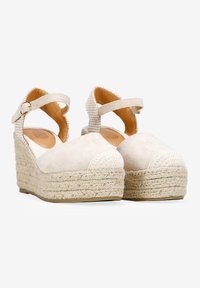 Sandalias de cuña beige con una correa de tela texturizada, acentuadas por una puntera redondeada y una plataforma de estilo espadrille trenzada. Correa en el tobillo ajustable.