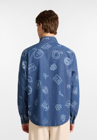 Korte mouwen denimbloes in donkerblauw, met lichtblauwe gestanste logo's en patronen verspreid over de stof. Klassieke kraag en met knopen afsluitbare manchetten.