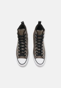 Pantofi sport înalte din piele ecologică verde măsliniu, cu sireturi negre și tălpi din cauciuc alb. Dispune de un guler căptușit și un design cu capac pe vârf.
