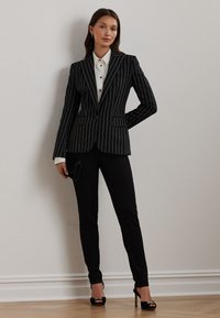 Melna pinstrīpa blazer ar atbilstošām pieguļošām melnām biksēm. Zem tā balta apkaklītes krekls. Melni augstpapēžu sandales. Vienkārša, eleganta prezentācija.