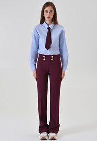 Chemise bleu clair avec une cravate, pantalon taille haute bordeaux foncé avec des boutons dorés, et baskets blanches avec des accents marron. Design simple.