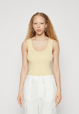 Lichtgele geribde tanktop met een vierkante halslijn, gecombineerd met witte broek met trekkoord en zijzakken.