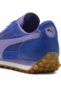 Sneakerissa on sininen ja violetti nubukki- ja synteettinen päällinen, pehmustettu kaulus ja tikattu kumipohja, jossa on pyöreitä nystyröitä.