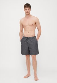 Bañador a rayas en gris oscuro y blanco, fabricado en tejido ligero, con cintura elástica y cordón ajustable, y bolsillos laterales.