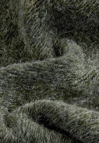 Textured green fabric with a soft, fuzzy surface, featuring a mix of dark and light fibers, creating a layered, intricate appearance.