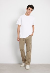 Witte T-shirt met korte mouwen gecombineerd met lichtbeige cargobroek met zijritszakken, vergezeld van witte sneakers. Eenvoudig, casual ontwerp.